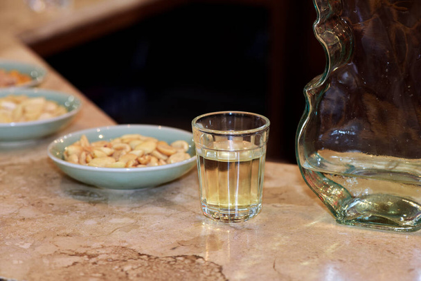 Vaso de pinga, un licor de caña de azúcar brasileño, con platos de aperitivos, en tabl bar
 - Foto, imagen