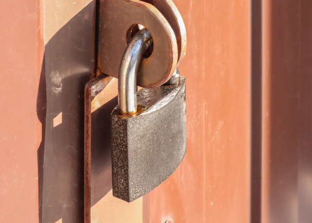 Close-up padlock on the gate of a metal brown fence made of modern siding, the concept of security. - Photo, Image