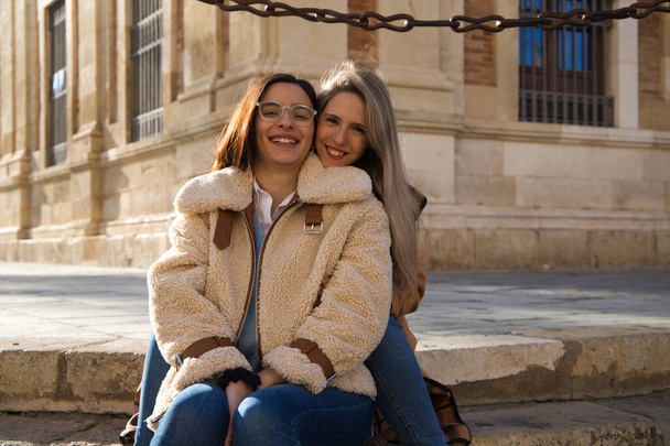古いヨーロッパの記念碑的な広場の舗装の階段に座っているレズビアンのカップル。彼らは愛と幸せの非常に多くです。概念観光と旅行、 lgtb 。権利と平等. - 写真・画像