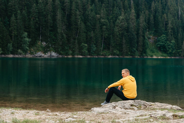 Traveler Man relaxing meditation with serene view mountains and lake landscape. Travel Lifestyle hiking concept summer vacations outdoor. Guy standing near the mountain Lake. A lonely man looks ahead - Photo, image