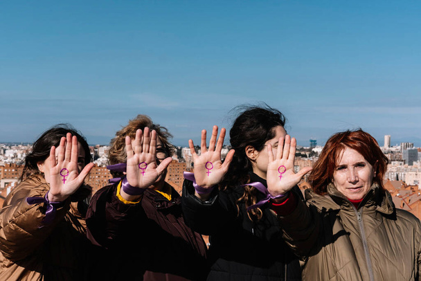 Cuatro mujeres de diferentes edades muestran la palma de sus manos con el símbolo feminista dibujado de una manera vengativa. Concepto feminista. Concepto de reclamación. - Foto, Imagen