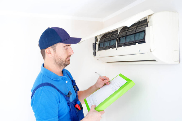 Tecnico con appunti guardando condizionatore d'aria per preventivo di installazione - Foto, immagini