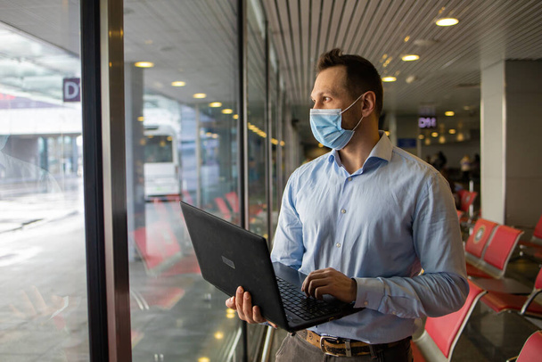 Passagier Geschäftsmann tragen Masken covid19 Krankheitsprävention und Telefonkonferenz mit Laptop während der Reise zur Arbeit im Ausland am Flughafenterminal. Neues normales und Geschäftsreisekonzept - Foto, Bild