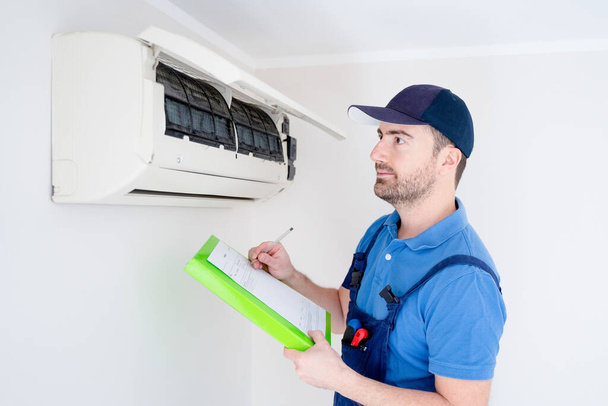 Technicus met klembord op zoek naar airconditioner voor installatie offerte - Foto, afbeelding