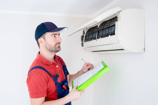 Technicus met klembord controleren airconditioner voor installatie schatting - Foto, afbeelding
