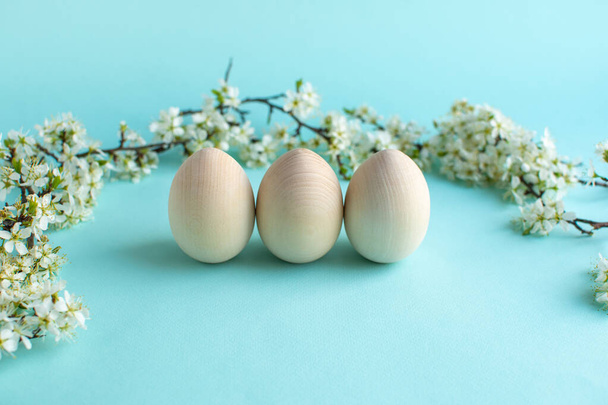 Happy Easter zero waste concept. Easter wood eggs with natural decor and fresh flowers. Christian religious Easter holiday on a blue background - Foto, Imagen