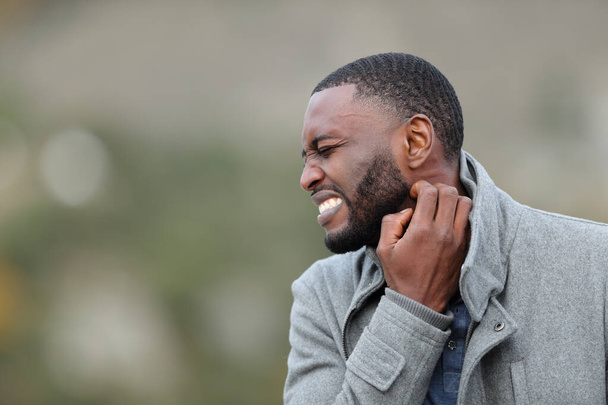 Stressed man with black skin scratching itchy neck in winter in a park - Foto, Bild