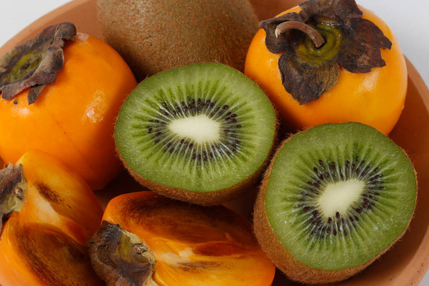 Still life with clay trough, persimmons and kiwis on the white background - Photo, Image