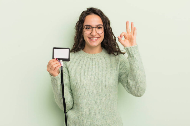 young pretty hispanic woman feeling happy, showing approval with okay gesture. accreditation card id - Foto, imagen