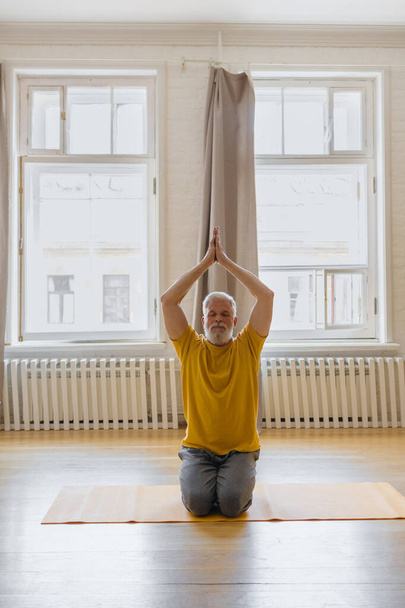 man with gray hair meditates and does breathing exercises. sports fitness and physical exercises for the elderly - Valokuva, kuva