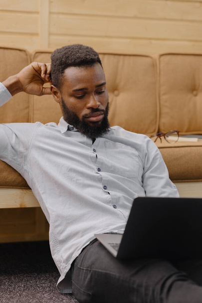 ein gutaussehender und junger afroamerikanischer Mann in einem Büro oder Coworking arbeitet an einem Laptop - Foto, Bild
