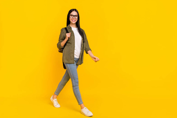 Full length photo of cute young lady go wear bag spectacles shirt jeans sneakers isolated on yellow background - Foto, afbeelding