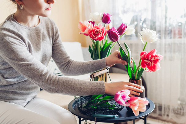 Woman arranges bouquet of tulips flowers at home. Housewife enjoys blooms in vases on table. Interior spring and decor - Photo, Image