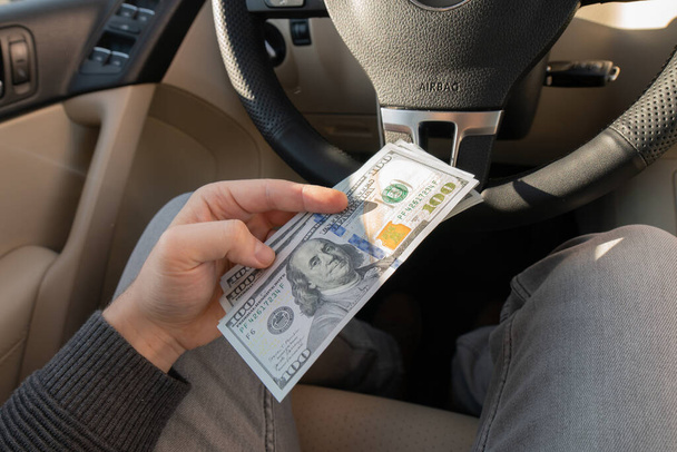 Un hombre con billetes de 100 dólares cerca del coche. Compra o alquila un auto nuevo. Finanzas concepto de dinero en coche - Foto, imagen