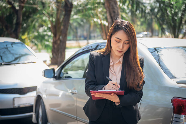 アジアの女性は、保険代理店が事故車事故報告書を書いていることを通知し、人々と交通保険の概念に. - 写真・画像