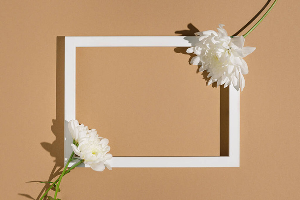 Composizione in stile minimale composta da fiori di crisantemo e cornice bianca su sfondo beige pastello. Concetto natura. Tema biglietto di auguri. Vista dall'alto. Posa piatta. - Foto, immagini