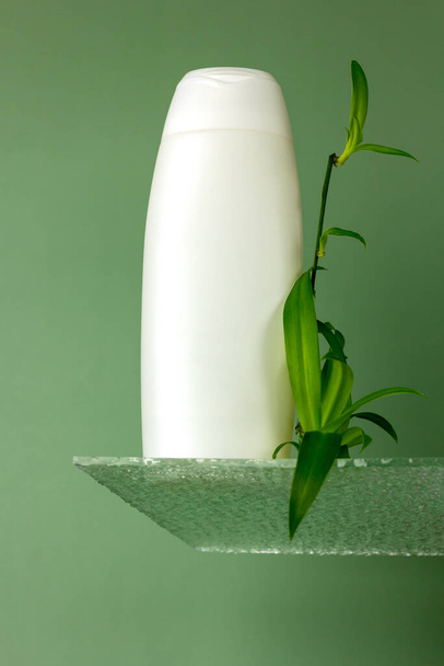 Creative composition with white bottle on a glass podium with plant leaves on a green background. Mockup for skincare products, natural cosmetics. Beauty concept for face and body care.  - Photo, Image