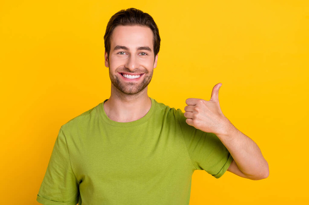 Photo of cool brunet hairdo millennial guy show thumb up wear green t-shirt isolated on bright yellow color background - Photo, Image