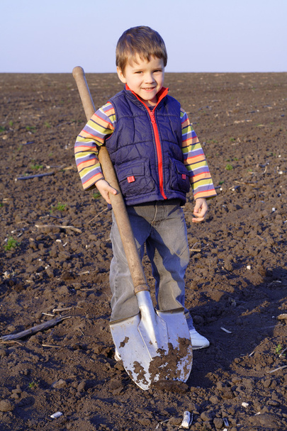 Pieni poika kaivaa kentällä iso lapio
 - Valokuva, kuva
