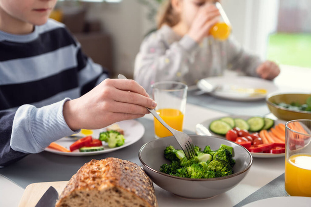 Children having breakfast: drinking orange juice and nailing fresh green broccoli on a fork - Photo, image