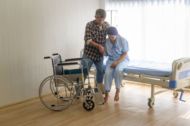 A Senior man helping cancer patient woman wearing head scarf moving to wheelchairs at hospital, health care and medical concept - Valokuva, kuva