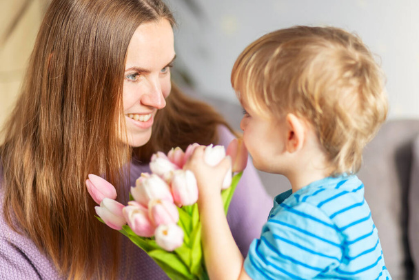 A cute son giving his mother a bouquet of tulips congratulating her on mother's day while celebrating the holiday at home. - Photo, Image