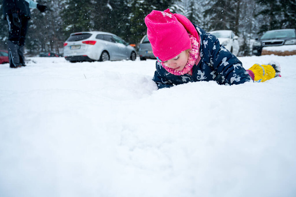 Cute girl examinating snow up close while lying on the ground. - Photo, Image