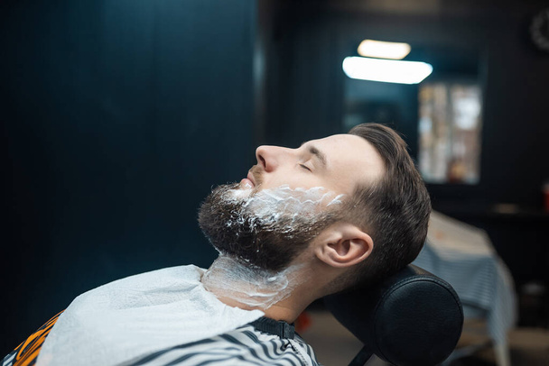 Человек с пеной для бритья на лице в парикмахерской - Фото, изображение