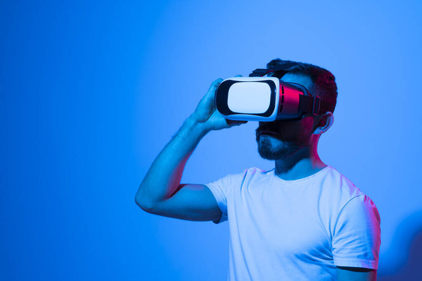 Closeup of young man wearing virtual reality goggles in modern studio with a neon light. Smartphone using with VR headset. Future technology concept. - Foto, Imagem