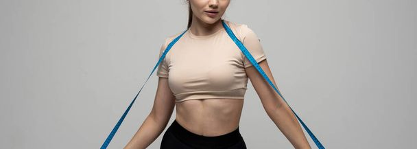 Sport fitness attractive young brunette girl in sportswear with blue measuring tape on her shoulder on white background Sports and diets. - Фото, зображення