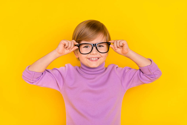 Photo of cute little boy with fair hair touch spectacles adjust them wear violet turtleneck isolated on yellow color background - Foto, immagini