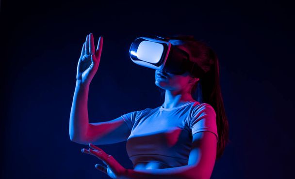 Future technology concept. Young woman wearing vr headset and watching 360 videos in neon light. Woman toching virtual objects in vr glasses. - Foto, Imagem
