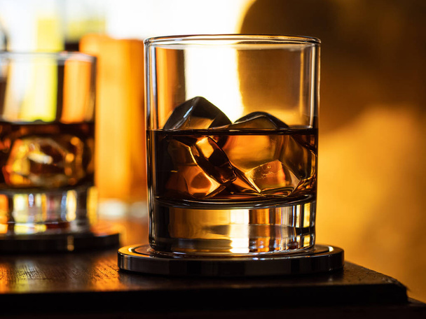 Glass of whisky on the rocks on a wooden bar top - Фото, изображение