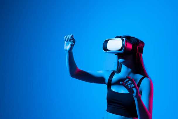 Brunette woman in a black t-shirt in VR headset looking up at the objects in virtual reality while playing a game or watching 3d movie and trying to touch it. Future technology concept. - Foto, Imagem