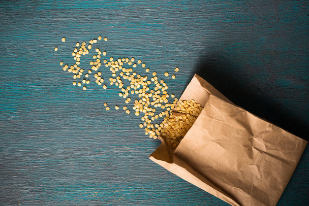 Paper bag with dry pepper seeds on wooden background - Фото, зображення