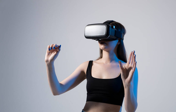 Amazed happy brunette girl in black t-shirt getting experience using VR headset glasses of virtual reality and exploring a new cyber worlds. - Photo, image