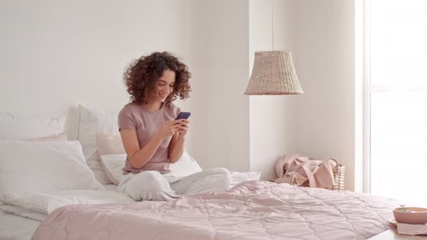 mujer joven usando móvil en el dormitorio - Metraje, vídeo