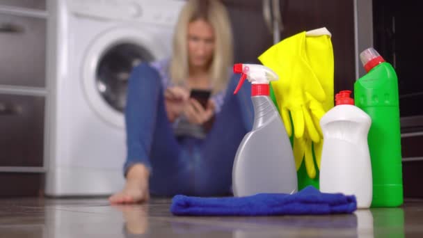 woman sitting on floor with her phone out of focus. Bottles of cleaning agent - Footage, Video