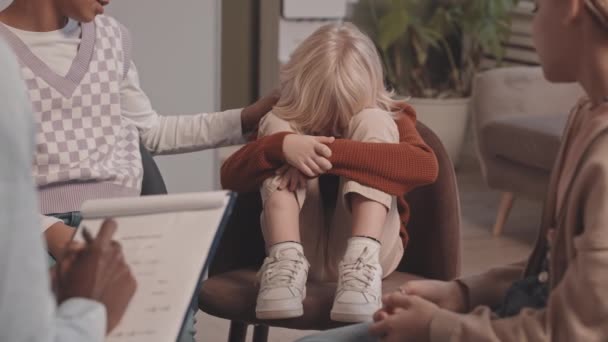 Slowmo πλάνο του μικρού Καυκάσιου αγοριού κλαίει σε συνεδρία ομαδικής θεραπείας, ενώ δύο διαφορετικά κορίτσια και αφροαμερικανός θεραπευτής τον παρηγορεί - Πλάνα, βίντεο