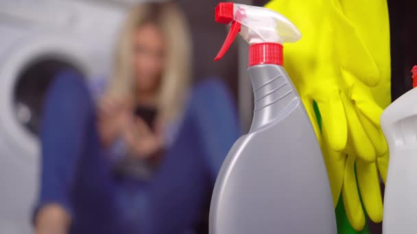 woman sitting on floor with her phone out of focus. Bottles of cleaning agent - Footage, Video