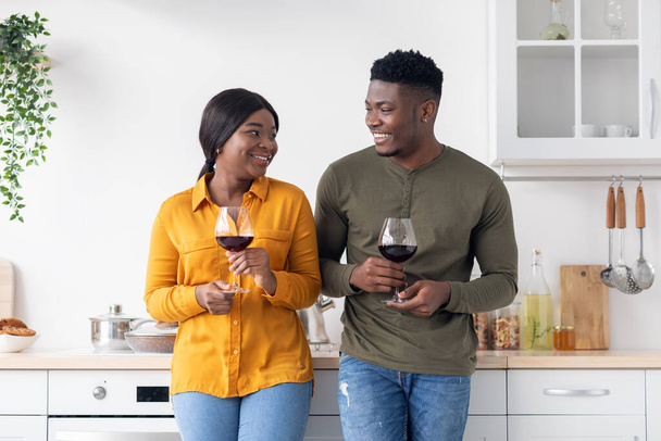 Внутренний роман. Счастливая чернокожая пара со стеклянными винами, стоящая в интерьере Китчен - Фото, изображение