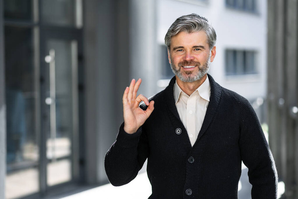 satisfecho positivo maduro de pelo gris hombre de negocios en la calle cerca del centro de negocios que muestra un buen gesto, recomienda - Foto, Imagen