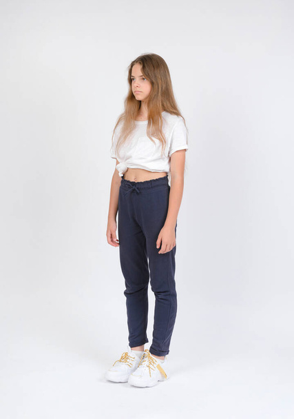1 white girl 11 years old in dark pants and a white T-shirt on a white background, model tests - Photo, Image