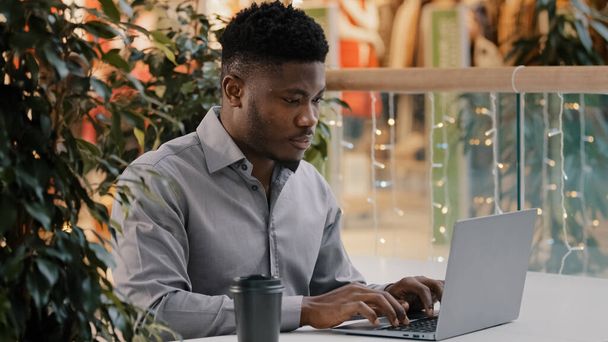 Freelancer masculino afro-americano focado olhando cuidadosamente para a tela do laptop trabalhando remotamente digitando e-mail de negócios escrevendo artigo conversando em rede social on-line usando aplicativo de computador - Foto, Imagem