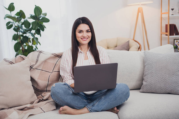 Portrait of attractive cheerful long-haired woman sitting on divan using laptop watching film video at home indoors - Фото, изображение