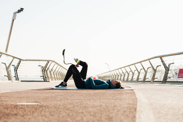 Young sportswoman with prosthesis doing exercise while working out on city bridge - Fotoğraf, Görsel