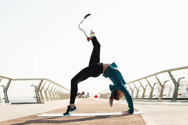 Young sportswoman with prosthesis doing exercise while working out on city bridge - Φωτογραφία, εικόνα