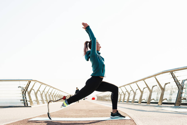 Giovane sportiva con protesi che fa esercizio mentre si allena sul ponte della città - Foto, immagini