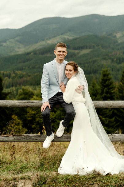 Beautiful newlyweds hug and smile being in nature. Portrait of the bride and groom in a lace dress. Wedding day of a happy couple of newlyweds. couple in the mountains - Zdjęcie, obraz