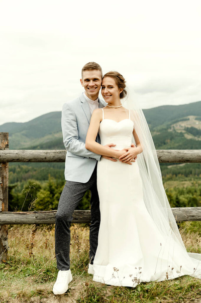 Beautiful newlyweds hug and smile being in nature. Portrait of the bride and groom in a lace dress. Wedding day of a happy couple of newlyweds. couple in the mountains - Φωτογραφία, εικόνα